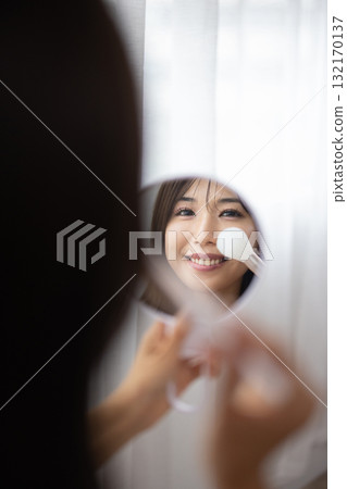 一位年輕女子一邊看著手鏡一邊化妝 132170137