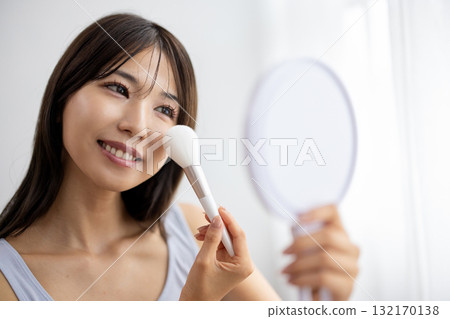 一位年輕女子一邊看著手鏡一邊化妝 132170138