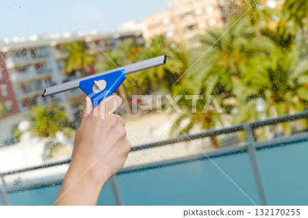 using a blue squeegee to clean a window 132170255