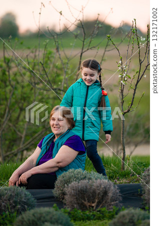 Grandmother and granddaughter enjoying time together outdoors amongst blooming plants. Grandmother and granddaughter enjoying time together outdoors amongst blooming plants. 132171002
