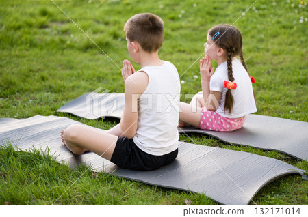 Children practicing mindfulness or yoga outdoors on mats. Peaceful moment of meditation in nature. 132171014