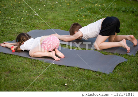 Children practicing yoga outdoors on mats. A relaxing and healthy activity for kids. 132171015