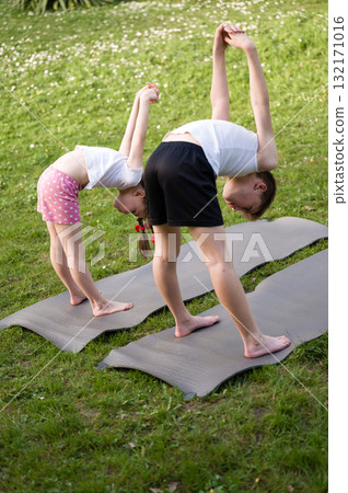 Kids practicing yoga outdoors on mats. Flexible and healthy children enjoying exercise in nature. 132171016