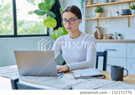 Teenage girl student sitting at the table with laptop, textbooks in home interior 132171776