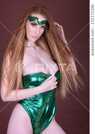Tall, beautiful, redhead model dressed in a shiny green leotard for Halloween, isolated against a dark background Tall, beautiful, redhead model dressed in a shiny green leotard for Halloween, isolated against a dark background 132172206