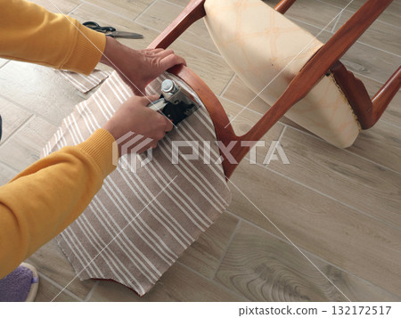 Anonymous person restore old vintage chair in home. Fabric replacement. Antique furniture and modern striped linen and cotton fabric. Hobbies, crafts, and retro-minimalist style. Anonymous person restore old vintage chair in home. Fabric replacement. Antique furniture and modern striped linen and cotton fabric. Hobbies, crafts, and retro-minimalist style. 132172517