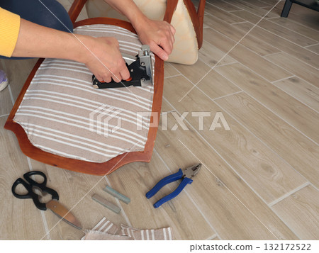 Anonymous person restore old vintage chair in home. Fabric replacement. Antique furniture and modern striped linen and cotton fabric. Hobbies, crafts, and retro-minimalist style. 132172522