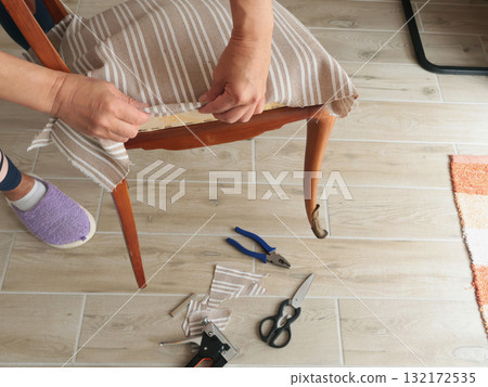 Anonymous person restore old vintage chair in home. Fabric replacement. Antique furniture and modern striped linen and cotton fabric. Hobbies, crafts, and retro-minimalist style. 132172535