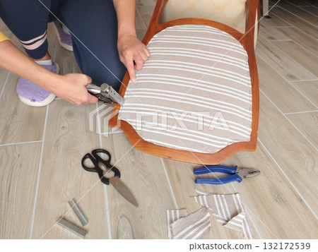 Anonymous person restore old vintage chair in home. Fabric replacement. Antique furniture and modern striped linen and cotton fabric. Hobbies, crafts, and retro-minimalist style. Anonymous person restore old vintage chair in home. Fabric replacement. Antique furniture and modern striped linen and cotton fabric. Hobbies, crafts, and retro-minimalist style. 132172539