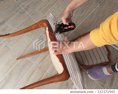 Anonymous person restore old vintage chair in home. Fabric replacement. Antique furniture and modern striped linen and cotton fabric. Hobbies, crafts, and retro-minimalist style. 132172565