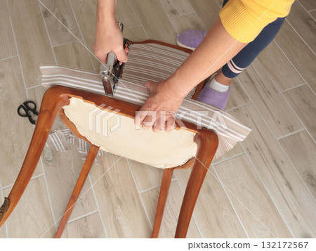 Anonymous person restore old vintage chair in home. Fabric replacement. Antique furniture and modern striped linen and cotton fabric. Hobbies, crafts, and retro-minimalist style. Anonymous person restore old vintage chair in home. Fabric replacement. Antique furniture and modern striped linen and cotton fabric. Hobbies, crafts, and retro-minimalist style. 132172567