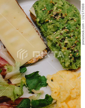 Nutritious morning meal featuring avocado toast sprinkled with seeds, cheese toast, scrambled eggs, and fresh green salad drizzled with vinaigrette on crisp white plate. Tasty and healthy breakfast Nutritious morning meal featuring avocado toast sprinkled with seeds, cheese toast, scrambled eggs, and fresh green salad drizzled with vinaigrette on crisp white plate. Tasty and healthy breakfast 132173808