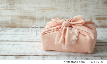 Wrapped Christmas gift in peach fabric, set against a rustic wooden backdrop. Japanese Furoshiki style, eco friendly, environmental gift wrapping concept. Place for text. Wrapped Christmas gift in peach fabric, set against a rustic wooden backdrop. Japanese Furoshiki style, eco friendly, environmental gift wrapping concept. Place for text. 132175183