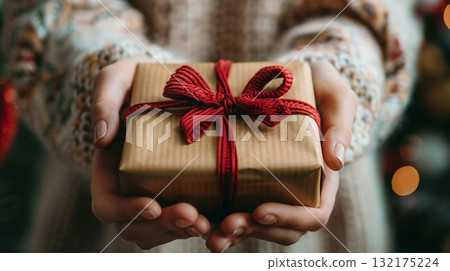 Christmas, New Year concept. A woman's hands hold gift with an red bow on Christmas background. Christmas, New Year concept. A woman's hands hold gift with an red bow on Christmas background. 132175224