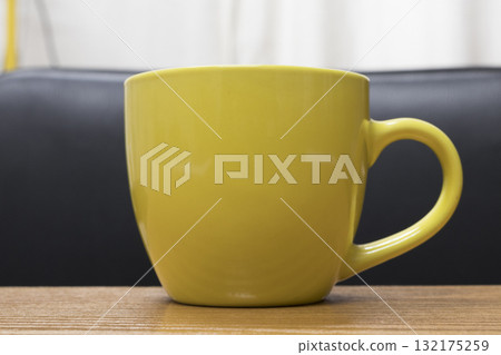 The yellow cup is located on a wooden surface. 132175259