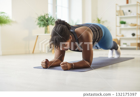 African American woman doing plank exercise, standing in plank position on fitness mat at home. African American woman doing plank exercise, standing in plank position on fitness mat at home. 132175397