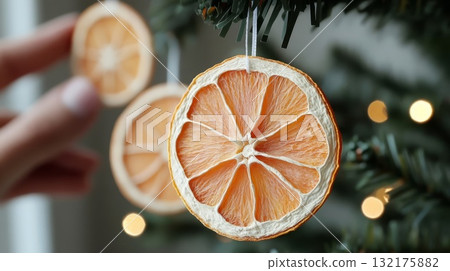 Hand placing dried orange slices on a green Christmas tree. Eco-friendly holiday decor, sustainable, holiday decor concept Hand placing dried orange slices on a green Christmas tree. Eco-friendly holiday decor, sustainable, holiday decor concept 132175882