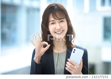 A businesswoman holding a smartphone and making an OK sign A businesswoman holding a smartphone and making an OK sign 132177231