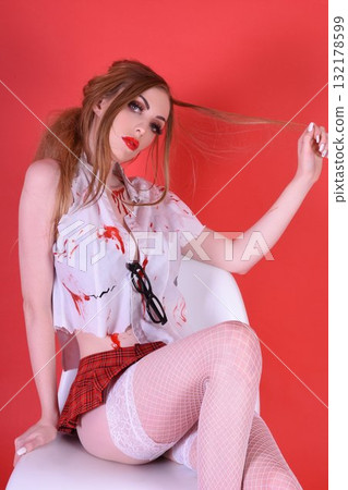 Shapely, redhead model dressed as a Zombie Schoolgirl for Halloween, isolated against a red background 132178599