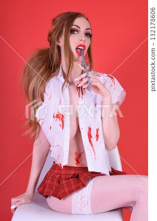 Shapely, redhead model dressed as a Zombie Schoolgirl for Halloween, isolated against a red background Shapely, redhead model dressed as a Zombie Schoolgirl for Halloween, isolated against a red background 132178606