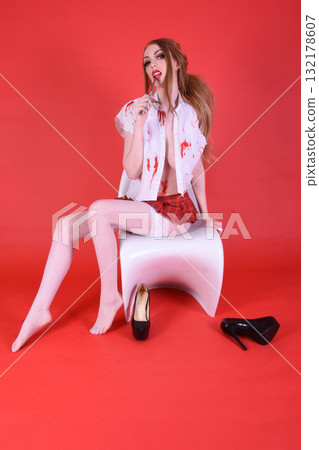 Shapely, redhead model dressed as a Zombie Schoolgirl for Halloween, isolated against a red background Shapely, redhead model dressed as a Zombie Schoolgirl for Halloween, isolated against a red background 132178607