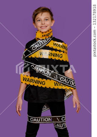 Boy stands with yellow warning tape wrapped around his body and mouth 132178918