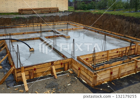 A concrete foundation is being poured on the construction site. Wooden formwork is used. A concrete foundation is being poured on the construction site. Wooden formwork is used. 132179255