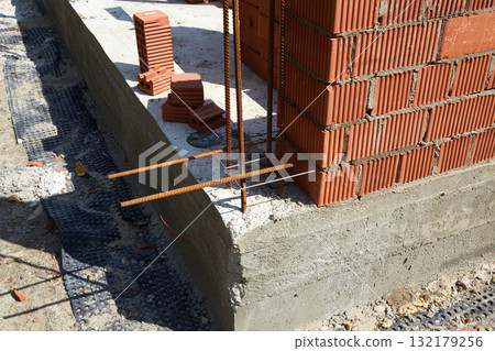 A construction site features a newly built brick wall with visible rebar bars extending from the concrete foundation. A construction site features a newly built brick wall with visible rebar bars extending from the concrete foundation. 132179256