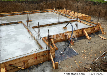 Construction of a concrete foundation with wooden forms at a building site on a cloudy day Construction of a concrete foundation with wooden forms at a building site on a cloudy day 132179260