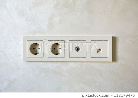 Electrical outlets and a network socket are neatly arranged on a light wall panel in a modern interior 132179476