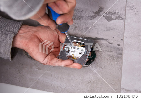 Electrician installing electrical outlets in a wall made of porcelain tiles. 132179479