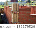 Brick walls are rising at a construction site, supported by wooden forms and metal rods. 132179529