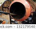A bright orange concrete mixer is surrounded by sand at a construction site. 132179540
