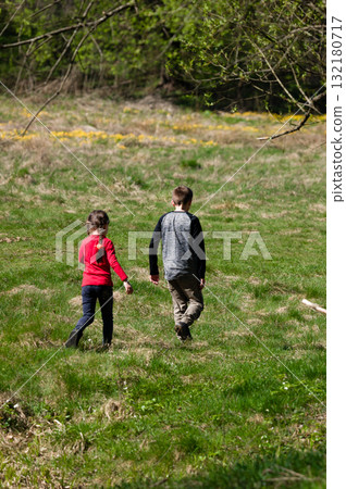 Two children walk away, exploring a sunny field. A carefree adventure in nature. 132180717