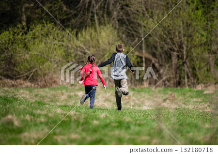 Two children run through a sunny field, enjoying a carefree day outdoors. Two children run through a sunny field, enjoying a carefree day outdoors. 132180718