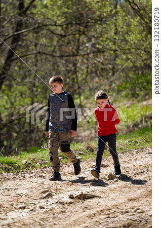 Boy and girl hiking on a dirt trail, enjoying a sunny day outdoors. 132180719