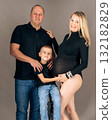Family portrait with pregnant woman, husband, and child in casual black outfits loving parents and son posing together in studio 132182829