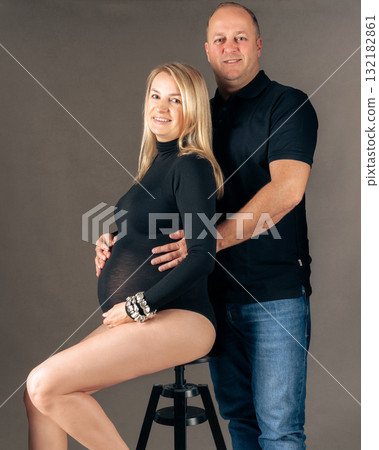 Pregnant woman and her husband posing in studio elegant maternity photo with loving couple awaiting baby Pregnant woman and her husband posing in studio elegant maternity photo with loving couple awaiting baby 132182861