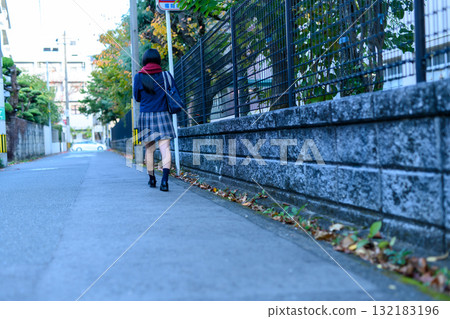 High school girl walking to and from school on a dark road for club activities on a cold day. High school student in winter clothes. Back view. 132183196