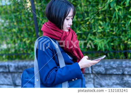 寒冷天氣裡使用智慧型手機上下學的高中女生 穿著冬裝上學的高中生 寒冷天氣裡使用智慧型手機上下學的高中女生 穿著冬裝上學的高中生 132183241