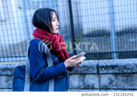 寒冷天氣裡使用智慧型手機上下學的高中女生 穿著冬裝上學的高中生 寒冷天氣裡使用智慧型手機上下學的高中女生 穿著冬裝上學的高中生 132183242