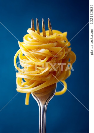 Close up studio photograph of a fork holding neatly twirled pasta against a vibrant blue background 132183625