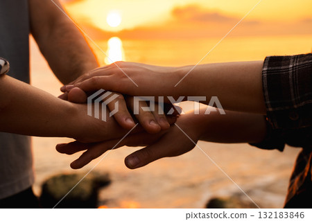 Close-up of three people joining hands in unity at sunrise on the beach, symbolizing teamwork, trust, and emotional connection 132183846
