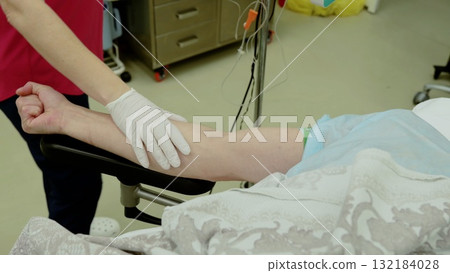 Medical professional adjusting patient's arm, donning sterile gloves during preoperative preparation in bright surgical environment Medical professional adjusting patient's arm, donning sterile gloves during preoperative preparation in bright surgical environment 132184028