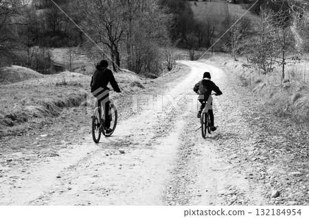 Two cyclists ride away on a gravel path, surrounded by trees and nature. Two cyclists ride away on a gravel path, surrounded by trees and nature. 132184954