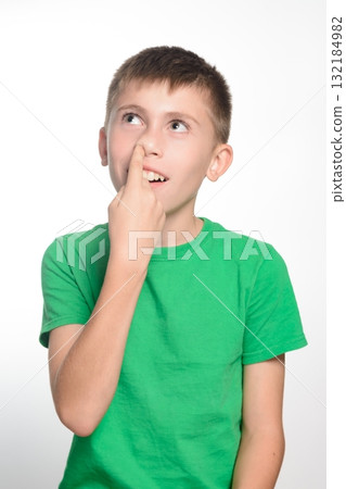 A boy in a green shirt playfully touches his nose, looking thoughtfully upward. 132184982