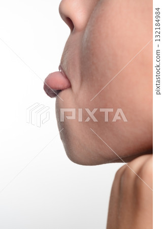 Close-up profile view of a person's face with their tongue sticking out slightly. The image is set against a plain white background. 132184984