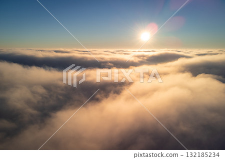 Aerial view of fluffy clouds with a sun on the horizon. Flying above the clouds 132185234