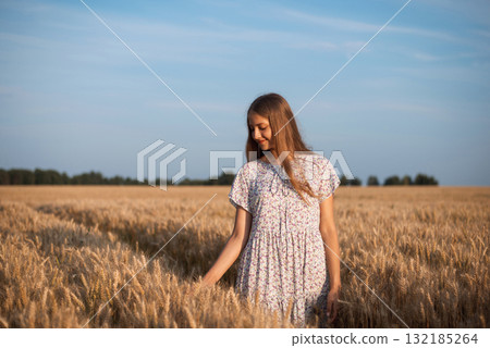 Portrait of a young girl having a walk in endless field of ripe rye. Evening calm atmosphere in the agricultural field Portrait of a young girl having a walk in endless field of ripe rye. Evening calm atmosphere in the agricultural field 132185264