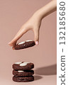 Hand reaching for chocolate cookies with white chocolate chips on a soft pastel background with copy space 132185680